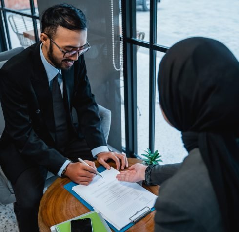 portrait of businessman signing an agreement letter during meeting with female muslim partner